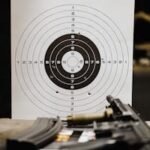 Close-up of a shooting target with bullet holes on a range table next to a rifle.